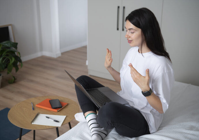 женщина на кровате в позе йоги держит на ногах ноутбук