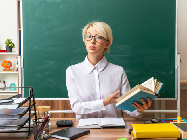 молодая учительница в очках сидит за столом